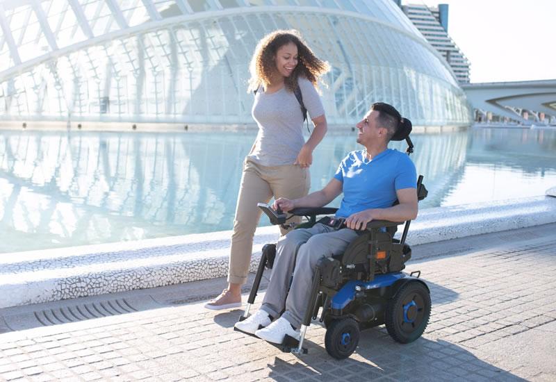 Man in electric wheelchair outside with woman walking alongside