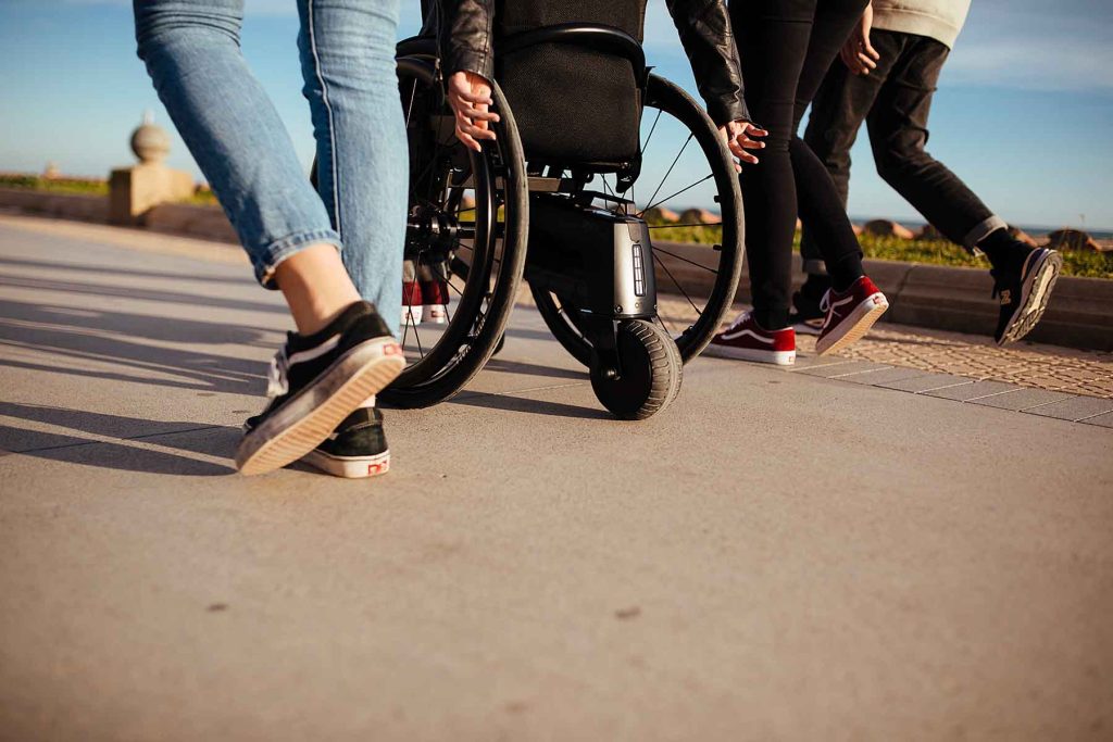 person in an Invacare wheelchair on a path, with friends walking alongside